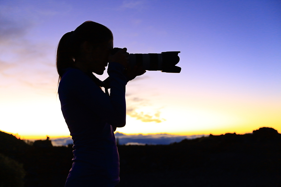 Photographer taking pictures with SLR camera at night. Nature landscape photographer with telephoto lens. Silhouette of woman taking photo after sunset.