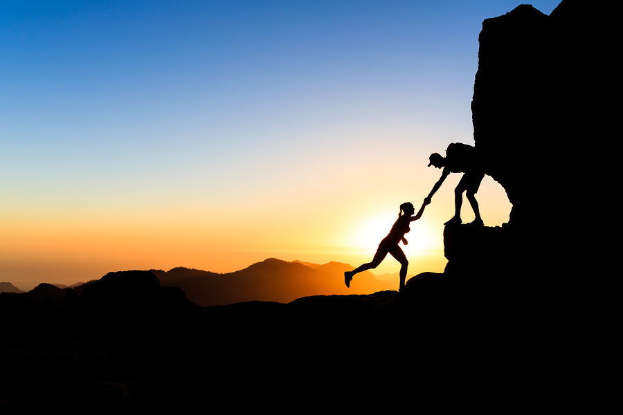 Teamwork couple helping hand trust help silhouette in mountains sunset. Team of climbers man and woman hikers help each other on top of mountain climbing together beautiful sunset landscape on Gran Canaria