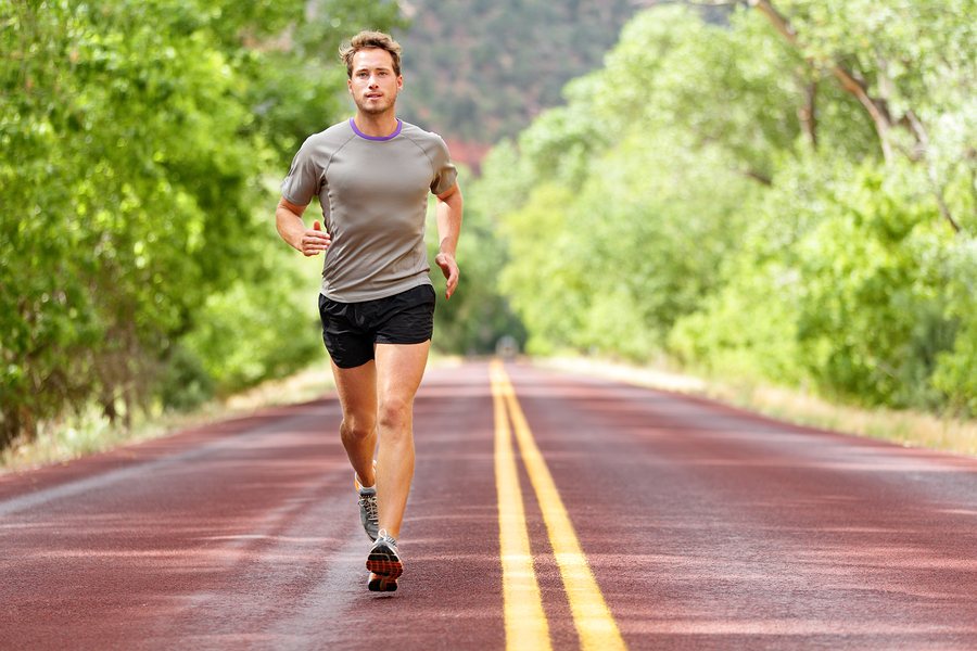 Sport and fitness runner man running on road training for marathon run doing high intensity interval training sprint workout outdoors in summer. Male athlete sports model fit and healthy aspirations.